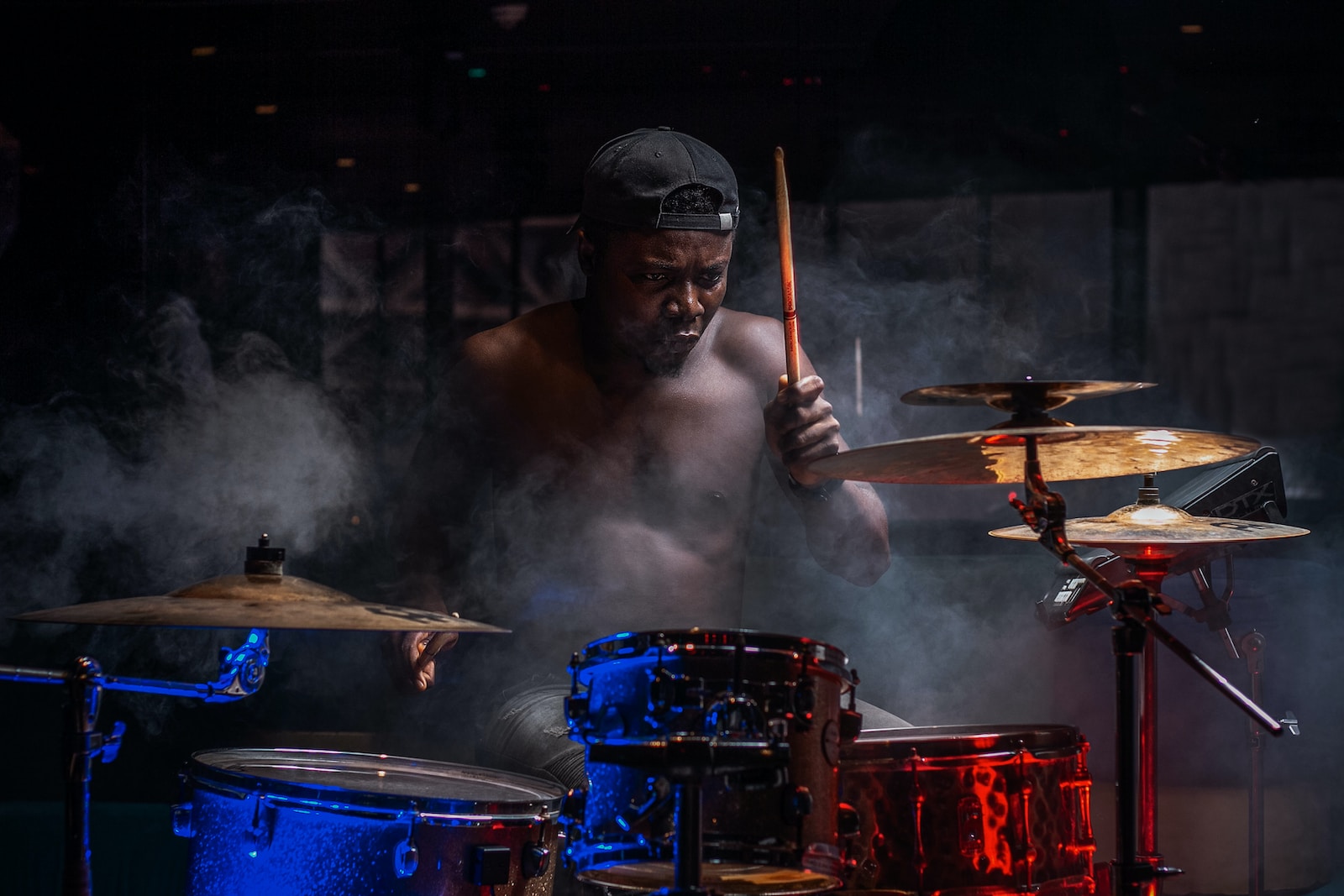 a shirtless man playing drums in a dark room